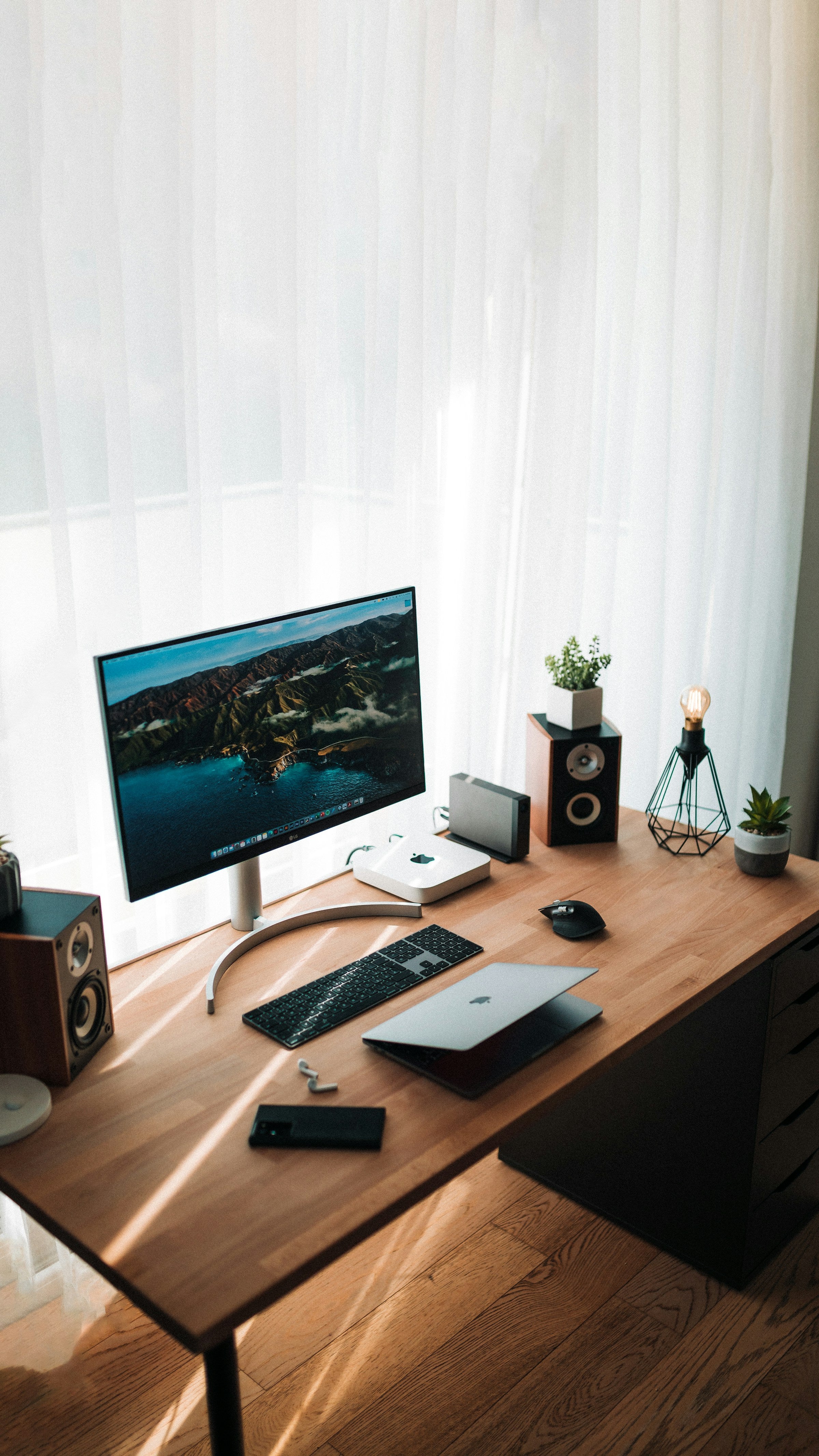 Warm minimalist wood desk setup with monitor and plant, sunlit window